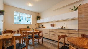 A modern kitchen with wooden cabinets, a central island, and a dining area with wooden tables and chairs. - The Ísafjörður Inn  (Isafjordur)