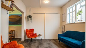 A modern living room with a blue sofa, an orange armchair, and a wooden bookshelf. - The Ísafjörður Inn  (Isafjordur)