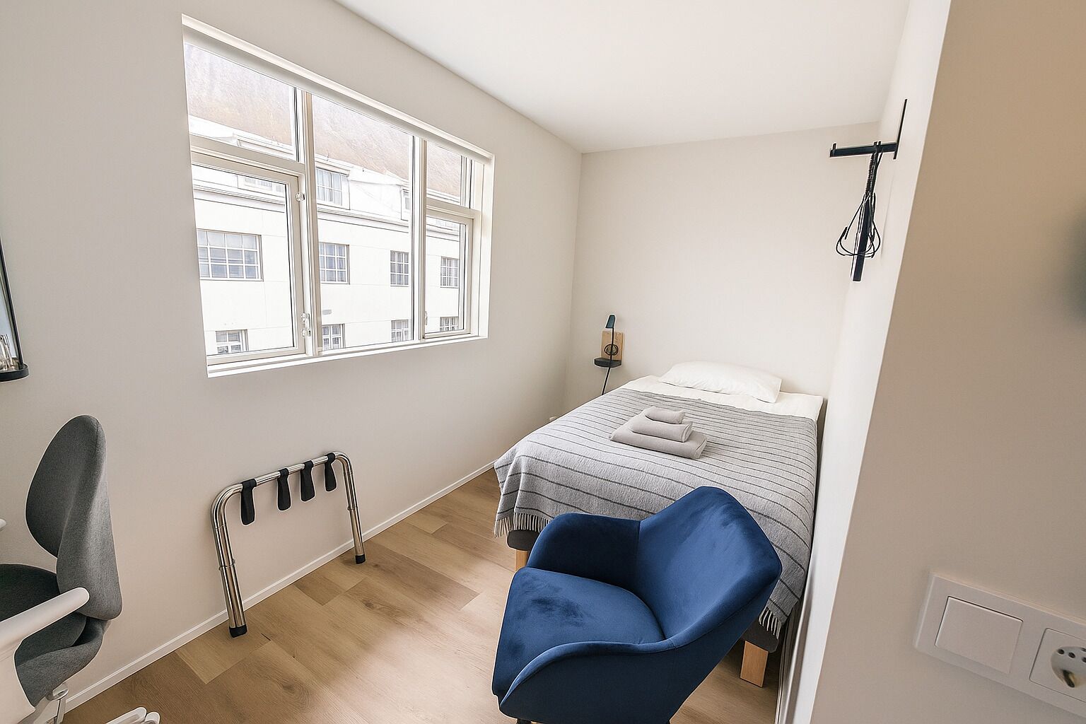 A bedroom with a bed, a chair, a radiator, and a window with a view of buildings.