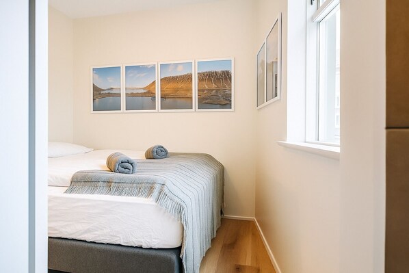 A bedroom with two beds, a window, and four framed pictures on the wall.