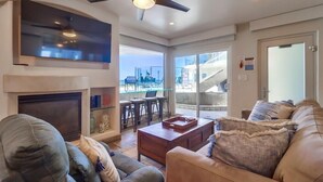 A spacious living room with a fireplace, comfortable seating, a large TV, and a view of the outdoors.