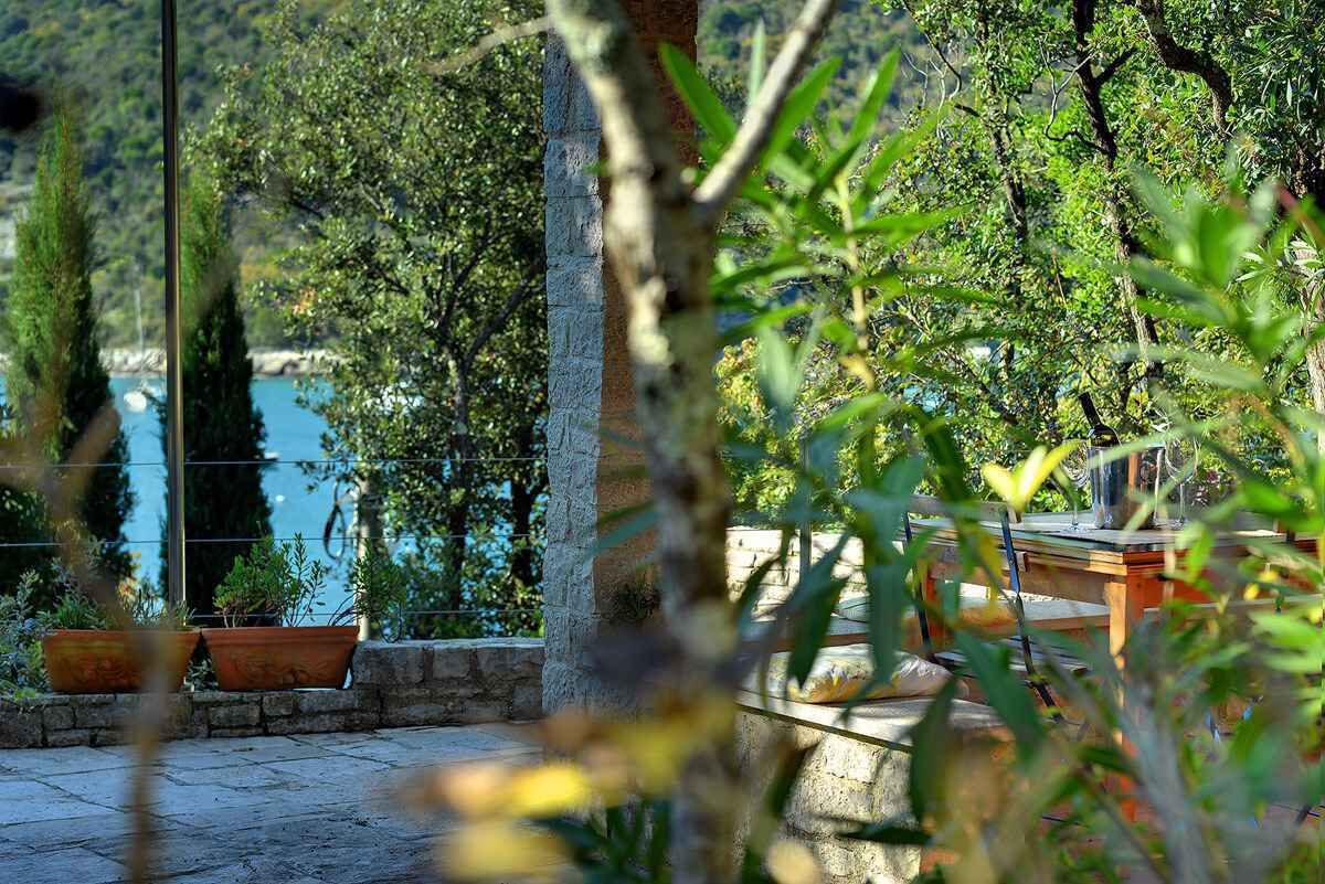 A stone patio with potted plants, a wooden table with a glass, and a view of a body of water.