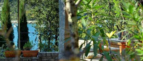 A stone patio with potted plants, a wooden table with a glass, and a view of a body of water.