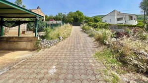 Ein gepflasterter Weg führt zu einem Gebäude, links mit einem überdachten Bereich und rechts ein weißes Gebäude.