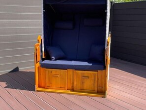 Eine Holzterrasse mit Schaukelstuhl, ausgestattet mit gepolstertem Sitz und Rückenlehne, sowie einem Sonnendach darüber.