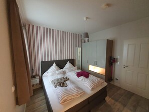 A hotel room with a bed, a wardrobe, a mirror, and a door. - Altstadtdomizil Wohnung Helin - Pure Entspannung in der Altstadt Borkums! - Alte Schulstraße (Borkum)