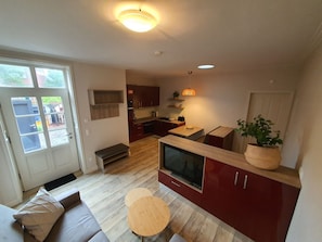 A compact living space with a kitchenette, a seating area with a sofa and a small table, and a large TV. - Altstadtdomizil Wohnung Helin - Pure Entspannung in der Altstadt Borkums! - Alte Schulstraße (Borkum)