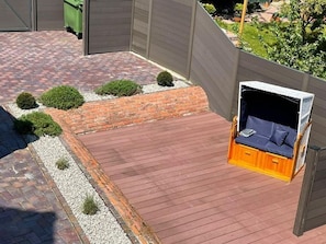 A wooden deck with a built-in seating area, surrounded by a brick wall and small bushes. - Altstadtdomizil Wohnung Helin - Pure Entspannung in der Altstadt Borkums! - Alte Schulstraße (Borkum)