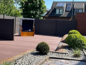 A backyard with a wooden deck, a barbecue area, and a small garden with a bush and gravel path. - Altstadtdomizil Wohnung Helin - Pure Entspannung in der Altstadt Borkums! - Alte Schulstraße (Borkum)