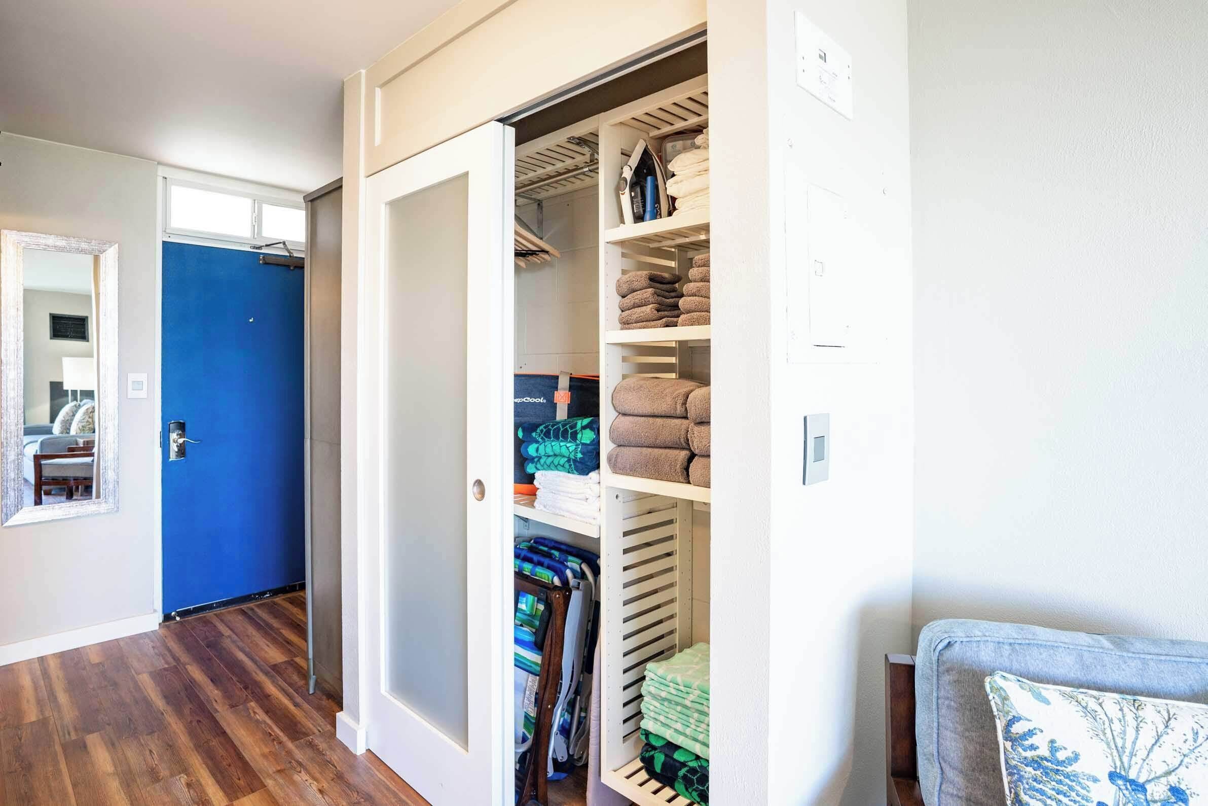 Un pasillo con una puerta azul, un armario con estantes y un sofá gris con un cojín estampado.