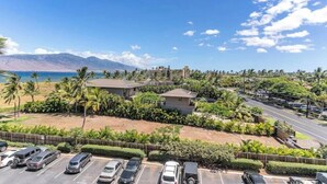 A coastal property with a parking lot, a road, and a view of the ocean and mountains. - Endless & Elegant Vistas (Kihei)