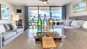 A hotel room with a dining table set with bottles, a wine glass, and a thank you card. - Endless & Elegant Vistas (Kihei)