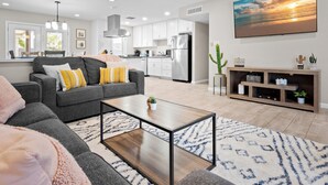 A modern living room with a grey sofa, a coffee table, and a large TV. - PuttPutt, Outdoor TVs & BBQ Bar, Pool & Spa! 5 mins from Old Town! (Scottsdale)