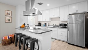 A modern kitchen with white cabinets, a stainless steel refrigerator, a built-in microwave, and a central island with bar stools. - PuttPutt, Outdoor TVs & BBQ Bar, Pool & Spa! 5 mins from Old Town! (Scottsdale)