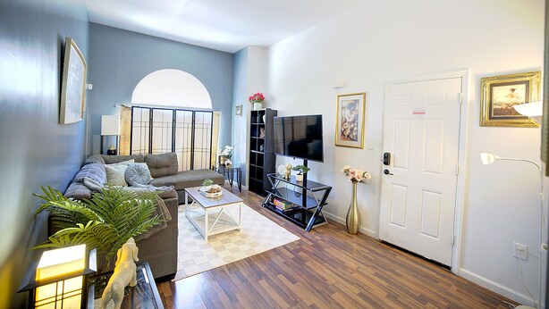 Uma sala de estar com sofá, mesa de centro, televisão e uma porta com moldura de quadro.