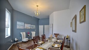 Uma sala de jantar com uma mesa comprida posta para seis pessoas, seis cadeiras, um candelabro e quadros nas paredes.