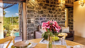 Un comedor con pared de piedra, una mesa dispuesta con platos y vasos, y un jarrón con flores.