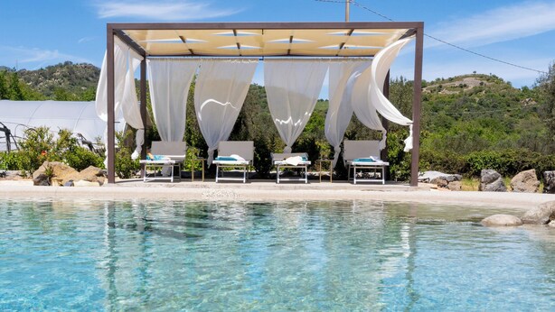 Un área junto a la piscina con una zona de estar cubierta y sillones de relax.