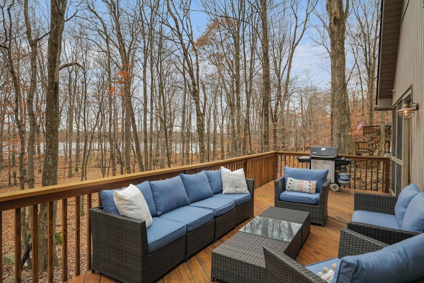 A deck with outdoor furniture, a grill, and a view of a forest.