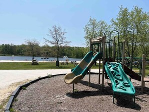 A playground with a slide and climbing structures near a body of water. - Wooded Lakeside adventure, walk to dock, 4 kid kayaks, screened porch, ping pong (Pocono Lake)