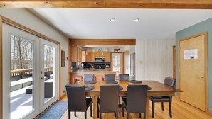 A modern kitchen with wooden cabinets, a dining table with chairs, and a view of a snowy deck through large sliding glass doors. - Wooded Lakeside adventure, walk to dock, 4 kid kayaks, screened porch, ping pong (Pocono Lake)