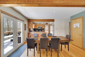 A modern kitchen with wooden cabinets, a dining table with chairs, and a view of a snowy deck through large sliding glass doors. - Wooded Lakeside adventure, walk to dock, 4 kid kayaks, screened porch, ping pong (Pocono Lake)