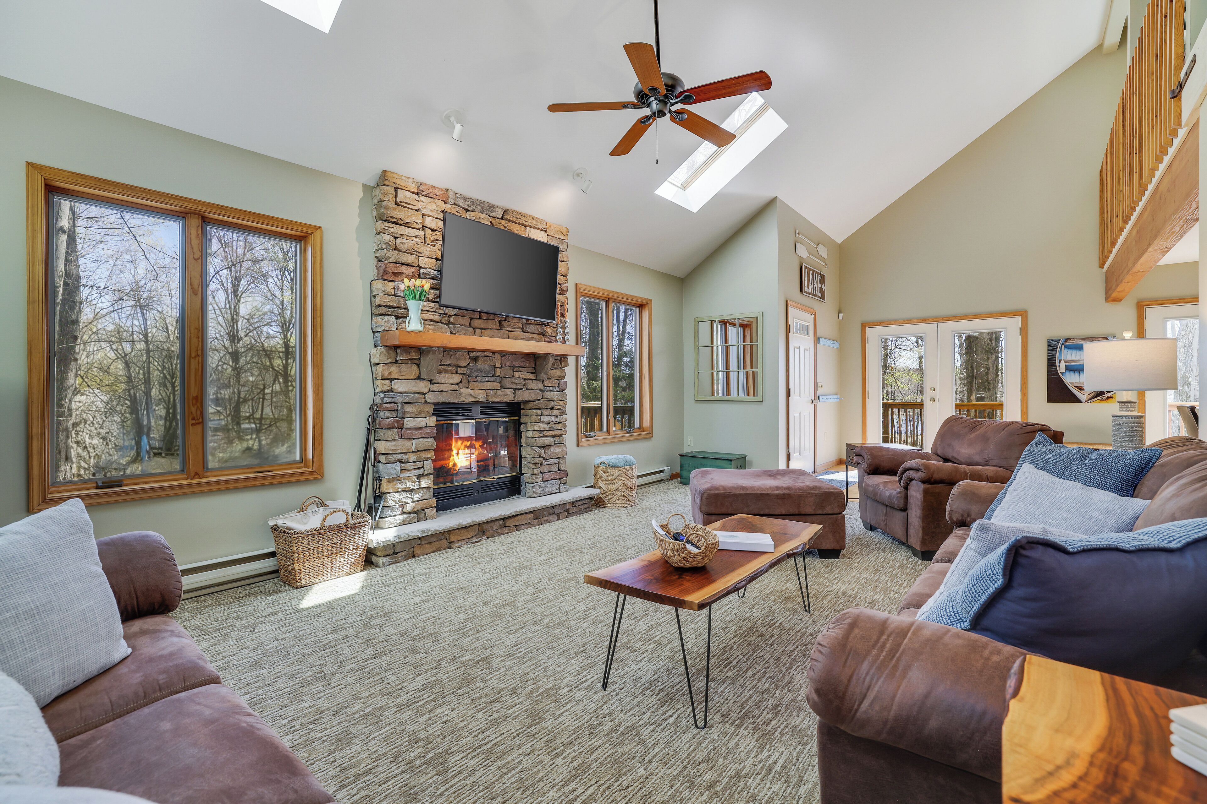A spacious living room with a stone fireplace, leather sofas, and a ceiling fan.