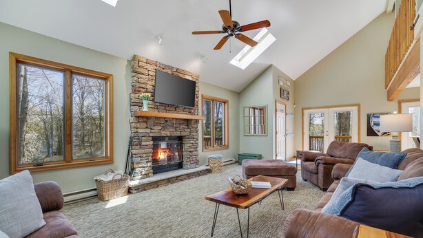 A spacious living room with a stone fireplace, leather sofas, and a ceiling fan. - Wooded Lakeside adventure, walk to dock, 4 kid kayaks, screened porch, ping pong (Pocono Lake)