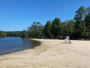 A sandy beach with a clear blue sky, trees, and a small structure. - Wooded Lakeside adventure, walk to dock, 4 kid kayaks, screened porch, ping pong (Pocono Lake)