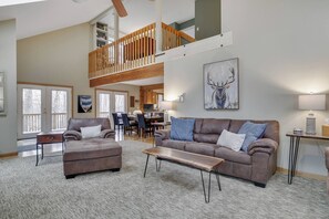 A spacious living room with a high ceiling, a wooden staircase, and a dining area. - Wooded Lakeside adventure, walk to dock, 4 kid kayaks, screened porch, ping pong (Pocono Lake)