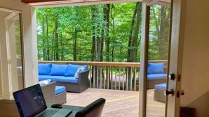 A room with a laptop on a table, a sofa, and a deck with a view of a forest. - Wooded Lakeside adventure, walk to dock, 4 kid kayaks, screened porch, ping pong (Pocono Lake)