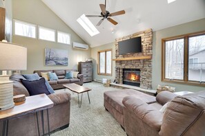 A living room with a fireplace, a ceiling fan, and a large window. - Wooded Lakeside adventure, walk to dock, 4 kid kayaks, screened porch, ping pong (Pocono Lake)