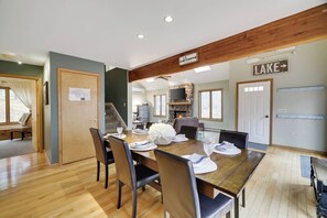 A dining area with a wooden table set for four, a stone fireplace, and a sign indicating a lake direction.