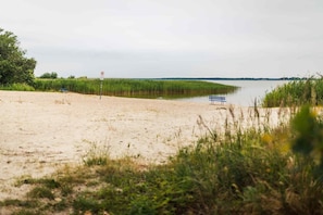 A beach with a bench, a sign, and a body of water. - Romantic vacation home at Baltic Lagoon Resort - 14b - Holiday homes Baltic (Fuhlendorf)