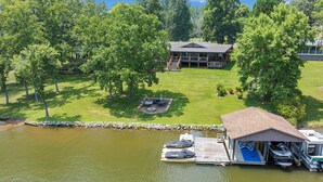 A lakeside property with a dock, a covered boat storage area, and a large house with a deck. - 7BR/5BA SML Lakefront – Walk to Private Dock w/ Boat Lifts, Fire Pit & Views! (Wirtz)