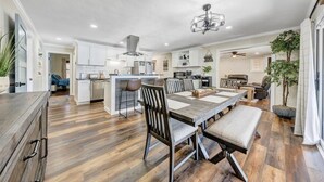 A spacious kitchen with a dining area, wooden flooring, and a ceiling fan. - 7BR/5BA SML Lakefront – Walk to Private Dock w/ Boat Lifts, Fire Pit & Views! (Wirtz)