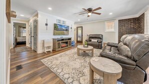 A living room with a fireplace, leather sofa, and a television. - 7BR/5BA SML Lakefront – Walk to Private Dock w/ Boat Lifts, Fire Pit & Views! (Wirtz)