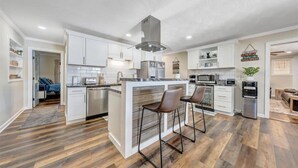 A modern kitchen with white cabinets, a central island with bar stools, stainless steel appliances, and a visible water dispenser. - 7BR/5BA SML Lakefront – Walk to Private Dock w/ Boat Lifts, Fire Pit & Views! (Wirtz)