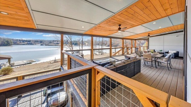 A deck with outdoor seating, a view of a body of water, and a covered area with a ceiling fan. - 7BR/5BA SML Lakefront – Walk to Private Dock w/ Boat Lifts, Fire Pit & Views! (Wirtz)