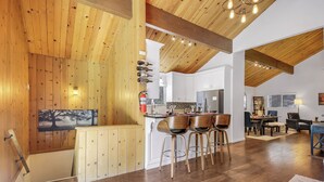 Une cuisine spacieuse avec des poutres en bois, un coin repas doté de tabourets de bar et une vue sur la salle à manger.