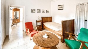 Quarto com uma cama, uma mesa redonda de madeira, uma cadeira vermelha, uma cadeira verde e uma pequena mesa de cabeceira.