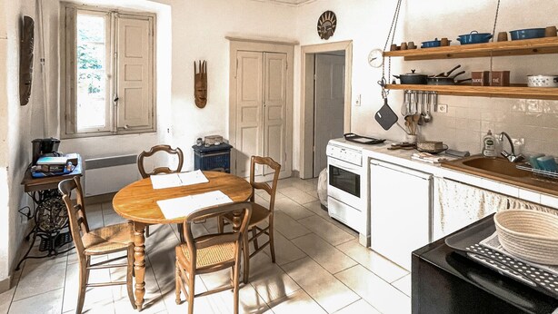 Uma cozinha com mesa de madeira, cadeiras, forno, pia e diversos utensílios.