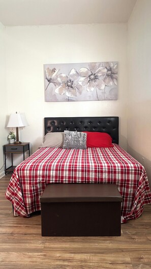 A bedroom with a bed, a nightstand, a lamp, a headboard, and a painting on the wall.