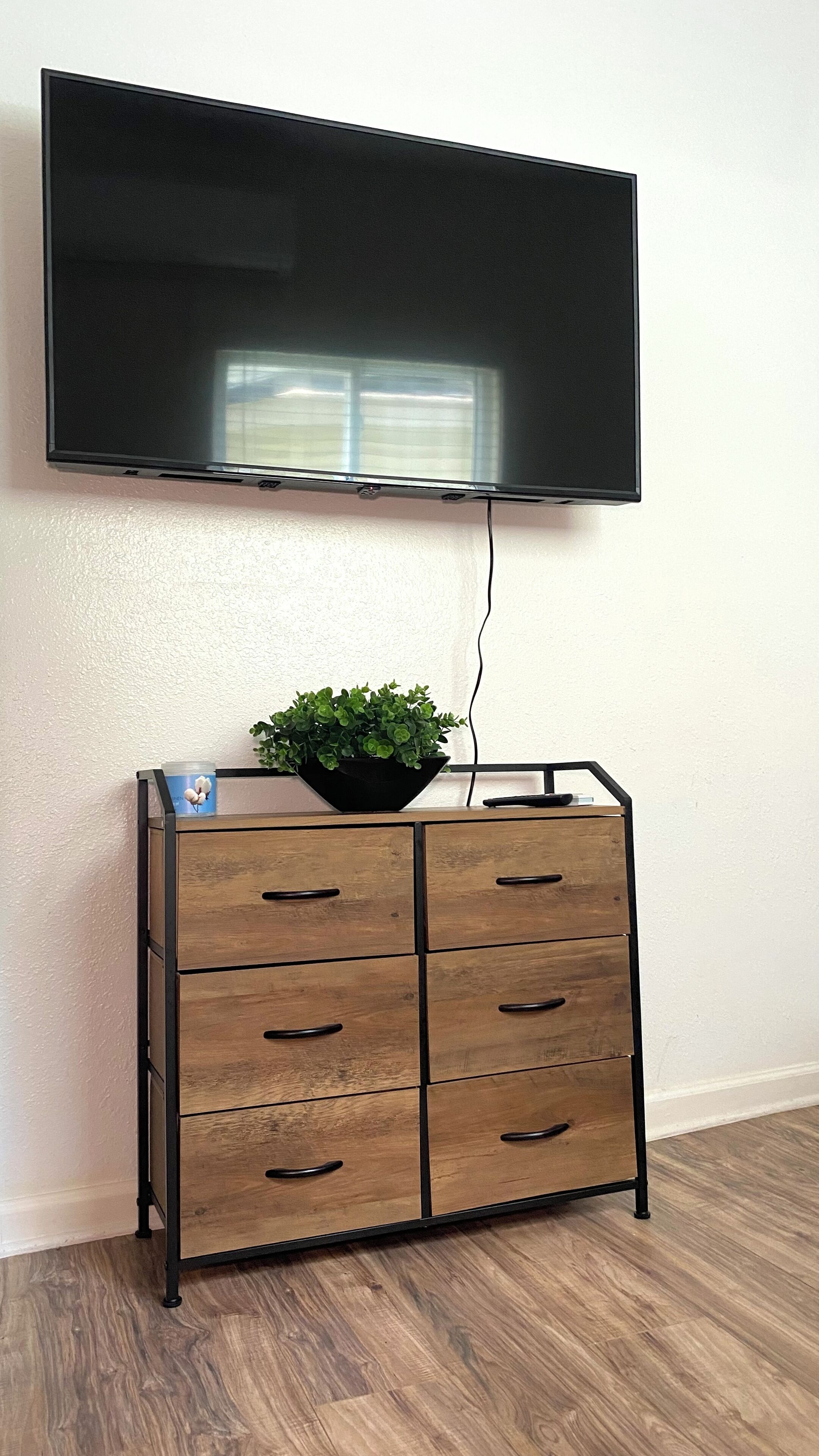 Un téléviseur à écran plat fixé au mur, au-dessus d’un meuble en bois doté de tiroirs.