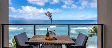A balcony with a wooden table, wicker chairs, a bottle of champagne, a potted plant, and a decorative orchid.