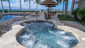 Een hottub omringd door lounge stoelen en een zwembad, met uitzicht op de oceaan en palmbomen.