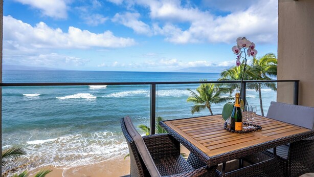 Een balkon met een houten tafel, rieten stoelen, een fles champagne en een glas.