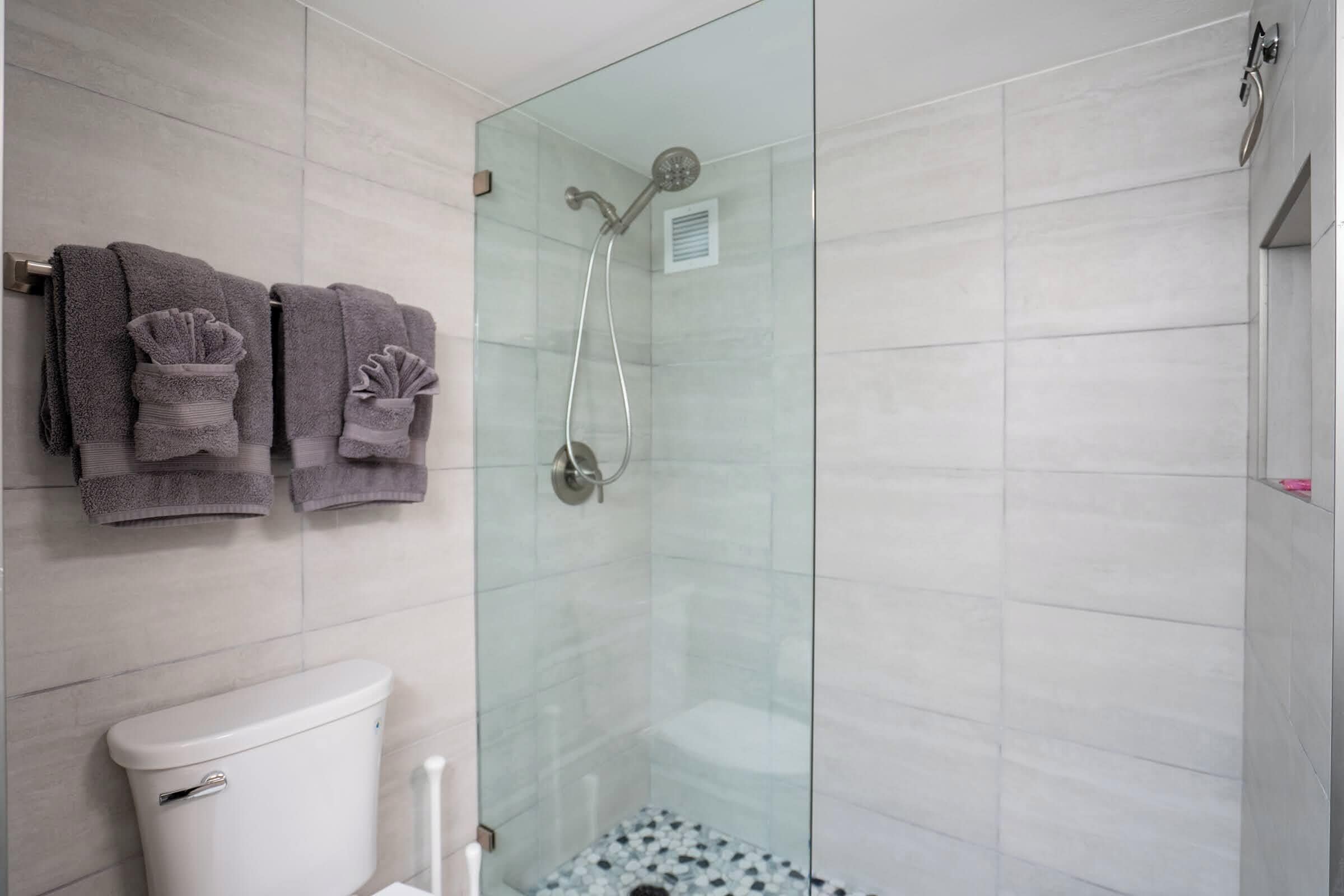 Un baño con ducha de vidrio, un inodoro y tres toallas colgadas en un perchero.