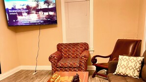 A living room with a wooden coffee table, a sofa, a patterned armchair, and a television mounted on the wall.
