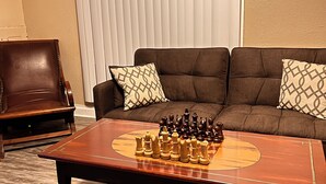 A living room with a brown leather armchair, a brown sofa with patterned cushions, and a wooden coffee table with a chess set.